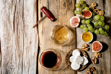 Glasses of red and white wine with grapes, figs, goat cheese and walnuts over old wooden background. Flat lay, copy space