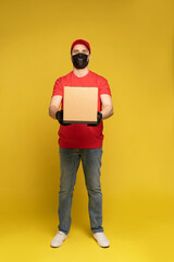 Delivery man in protective mask and gloves with box in studio isolated on yellow background