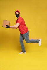 Delivery man in protective mask and gloves with box in studio isolated on yellow background