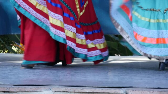 Latino women in colourful traditional dresses dancing Jarabe tapatio, mexican national folk hat dance. Street performance of female hispanic ballet in multi colored ethnic skirts. Girls in costumes.