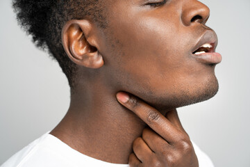 Closeup of afro man touches fingers of sore throat, isolated on gray background. Thyroid gland,...