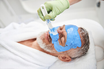 Fototapeta premium Spa worker putting blue cream on a person face