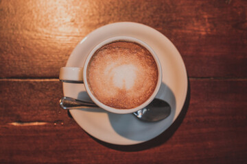 Taza de café con leche en un plato blanco sobre una mesa de madera con una cuchara de plata 