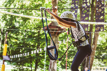 Naklejka premium Little girl with safety equipment at the forest adventure park, amusement center for children outdoor
