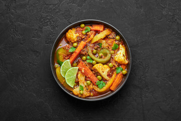 Veg Kolhapuri in black bowl on dark slate table top. Indian vegetable curry dish. Vegetarian asian food and meal. Top view