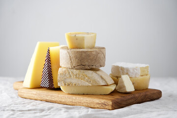 Various kind of cheese served on wooden board, traditional pieces of Spanish, French, Italy cheese. Light background with copy space, table with gray linen tablecloth