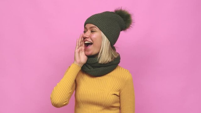 Young cute woman winter clothes shouting and holding palm near opened mouth