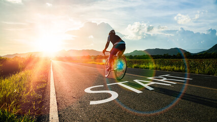 Concept of start straight and beginning for cooperation.Blurry Man ride on bike and word start written on the road at sunset add lens flare.Concept of challenge or career path,business strategy. - obrazy, fototapety, plakaty