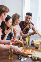 excited multicultural friends eating pizza and drinking beer during party