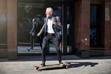 Grey-haired man riding a longboard in town