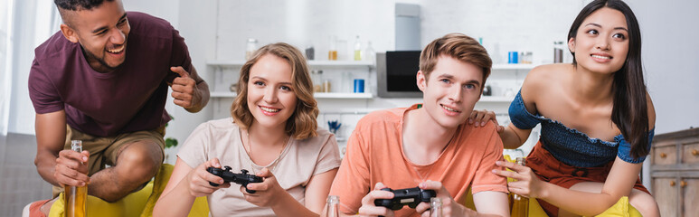 KYIV, UKRAINE - JULY 28, 2020: horizontal image of multicultural friends playing video game during party in kitchen