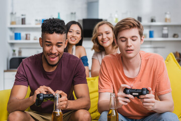 Obraz premium KYIV, UKRAINE - JULY 28, 2020: multicultural friends playing video game during party in kitchen