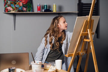 cute girl artist draws her oil painting from a reference from a laptop