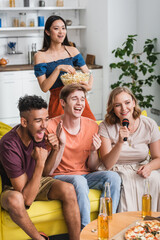 excited multiethnic friends applauding while singing karaoke during party
