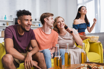 selective focus of asian woman holding bowl of popcorn while multicultural friends singing karaoke