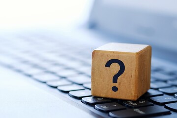 A question mark on a wooden cube on a computer keyboard, with a blurred background and shallow...