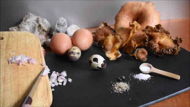 Zutaten f&uuml;r R&uuml;hrei mit Pilzen, Eier, Wachteleier, Schwammerl, Salz, Pfeffer und Zwiebel auf schwarzes Brett streichen vor silbernem Hintergrund mit Steinen