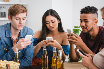 selective focus of multicultural friends chatting on smartphones near beer during party
