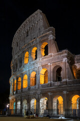 Fototapeta premium Colosseum at night. Night view of the famous monument, the ancient Flavian Amphitheater, with the arches illuminated by the artificial yellow lights in the dark of the night.