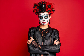 Young creepy lady calavera. wears artistic make-up for the feast of all the dead. dressed in a black leather jacket with a wreath of flowers on her head.Symbol of the Day of the Dead isolated in red.