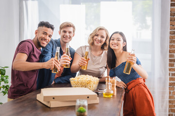 joyful multiethnic friends looking at camera while holding bottles of beer