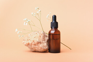 A glass bottle with aromatic oil or serum on a stone and little twig with flowers near. Natural...