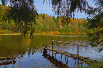 Autumn landscape. Old wooden bridge with handrail on the lake shore.