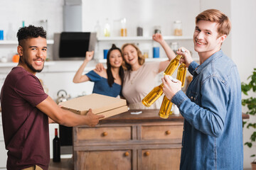 Fototapeta premium selective focus of multicultural friends holding pizza boxes and beer near women showing yeah gesture