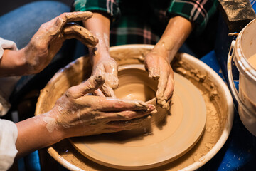 close-up of the hands of a potter's girl and a child who are sculpting clay dishes on a potter's wheel