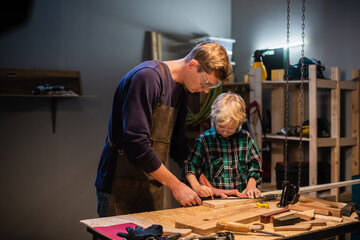 an experienced carpenter and his young apprentice make wood crafts in their workshop