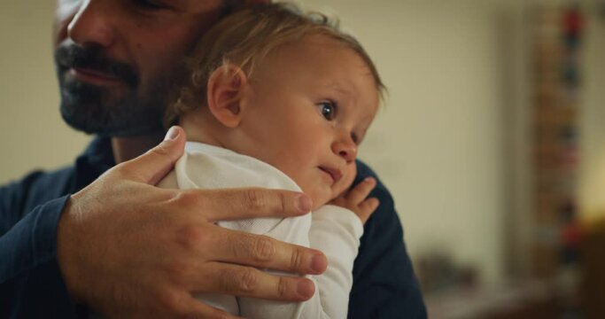 Authentic close up shot of an young happy smiling father is keeping in arms his son toddler baby boy and cuddling he while enjoying time together at home.