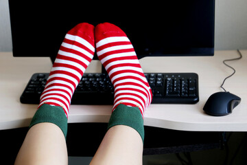 Female feet in Christmas socks on the office desk with PC and keyboard. Concept of New Year...