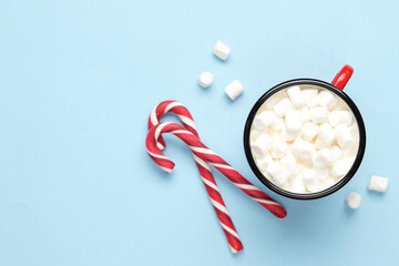 Hot drink with marshmallows and сandy cane in red cup on pastel blue background. Holiday festive celebration greeting card with copy space