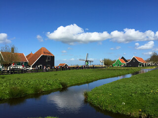 Fototapeta na wymiar dutch historic windmills on meadow near the river at blue sky, in Zaanse Schans, North Holland, Netherlands