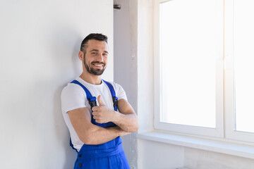 A constructor in blue overalls stands against the wall and poses