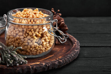 Pine nuts in a glass dish on a dark background with nuts scattered around