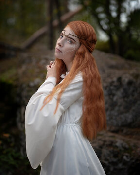 Young red-haired woman in a white dress in a pine forest