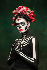 Scary. Young girl like Santa Muerte Saint death or Sugar skull with bright make-up. Portrait isolated on dark green studio background with copyspace. Celebrating Halloween or Day of the dead.