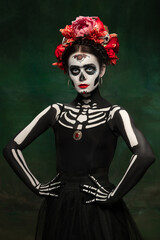 Scary. Young girl like Santa Muerte Saint death or Sugar skull with bright make-up. Portrait isolated on dark green studio background with copyspace. Celebrating Halloween or Day of the dead.