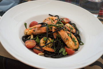 Closeup of shrimps , tomatoes and seaweed pasta in a white plate at the restaurant terrace in the street