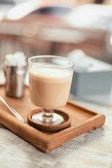 Hot raf coffee in a glass stylish cup on a wooden board in a street cafe on a park background. Morning coffee on the terrace in cafe
