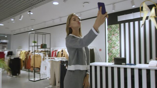 Pretty woman is taking a selfie dressed in grey suit at clothing store, tracking shot, 360 degree