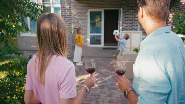 selective focus of couple holding glasses of wine near kids and new house