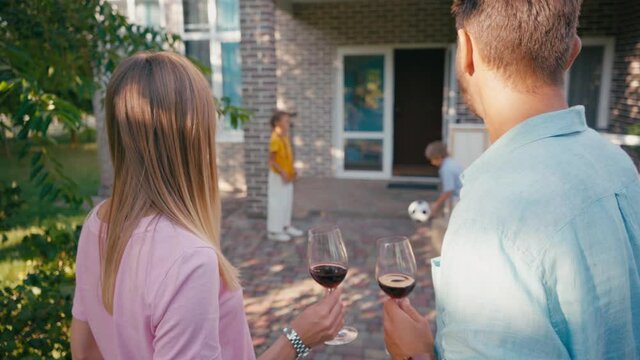 selective focus of couple holding glasses with wine near kids and new house