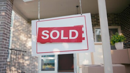 cropped view of man putting sticker with sold lettering on sale board near house