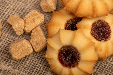 Homemade pastry cookies with jam and pieces of brown cane sugar on a background of homespun fabric with a rough texture, close-up, selective focus.