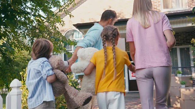 parents walking and holding hands with kids near new home