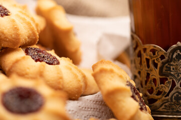 Homemade pastry cookies with jam and a faceted glass of tea in a vintage Cup holder on a background of homespun fabric with a rough texture, close-up, selective focus.