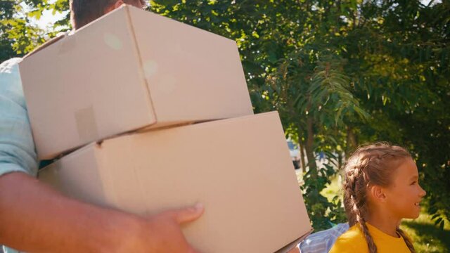parents holding boxes and plant while walking with children, relocation concept