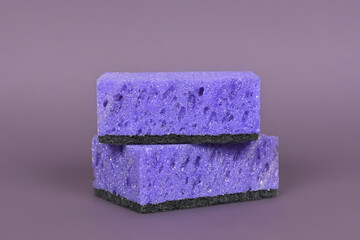 A porous purple washcloth for cleaning the apartment and washing dishes on a gray background.